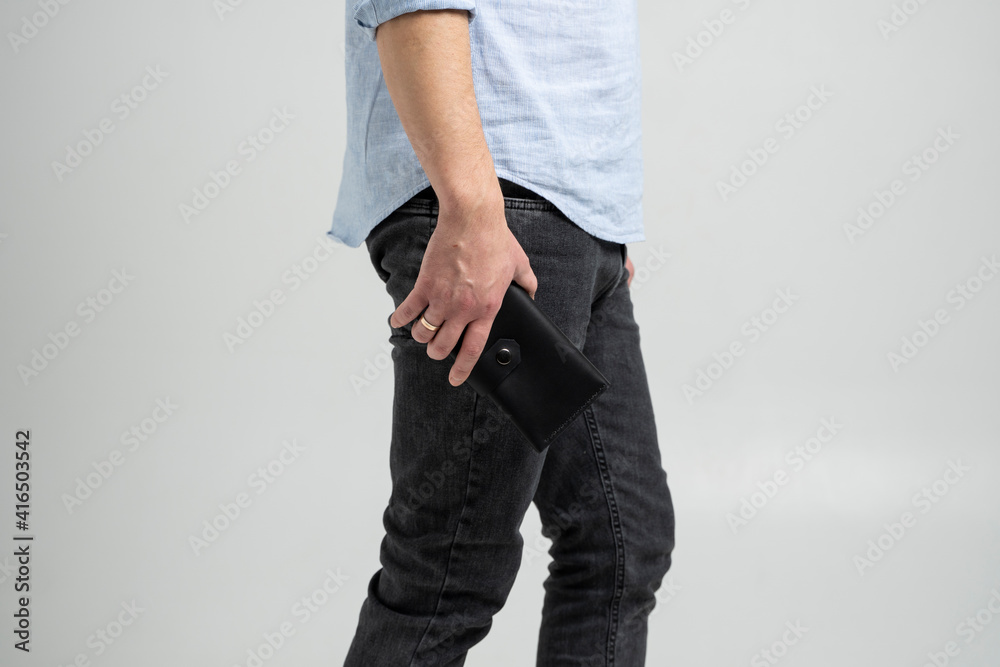 Stylish handmade black leather wallet in a mens hand in blue shirt and black jeans on white background. Stylish handmade black leather wallet in a mens hand in blue shirt and black jeans on white background.