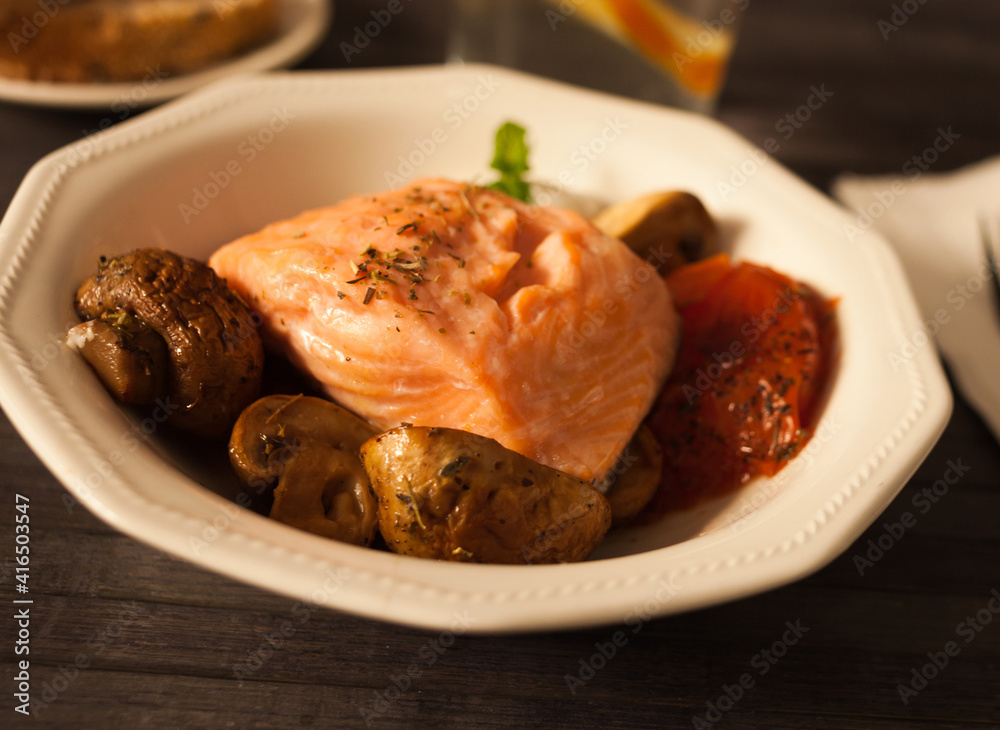 steamed sea trout fillet served on fried mushrooms with tomatoes in a white bowl