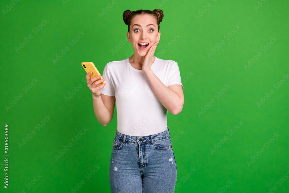 Photo portrait of amazed female teenager touching cheek holding mobile phone isolated on vibrant green color background Photo portrait of amazed female teenager touching cheek holding mobile phone isolated on vibrant green color background