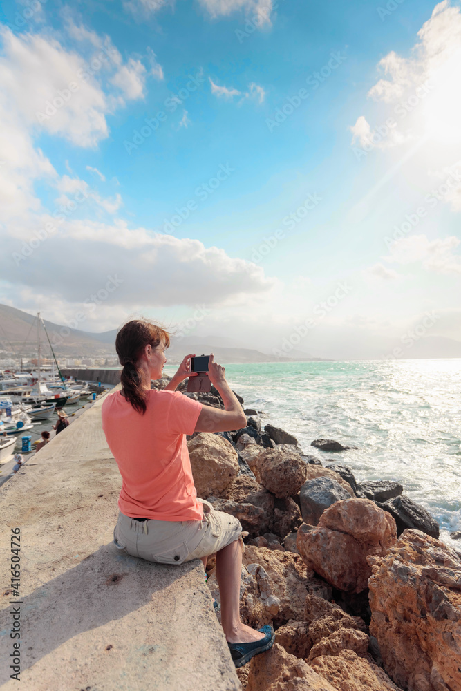 An attractive female traveler uses her mobile phone to photograph a beautiful seascape.