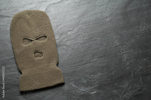 Beige knitted balaclava on black table, top view. Space for text