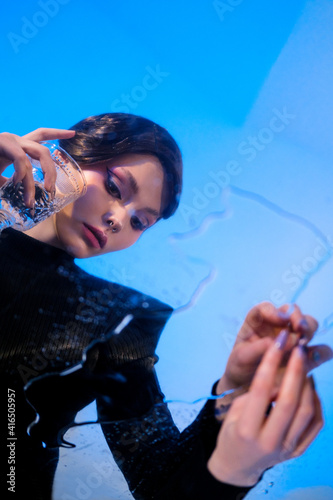 A beautiful young beautiful female model poses in the studio. Blue light, reflected in a flexible mirror, glass and light pattern in the background.