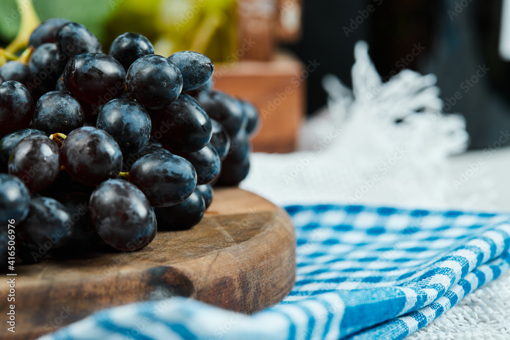 A cluster of black grapes on wooden plate with blue tablecloth