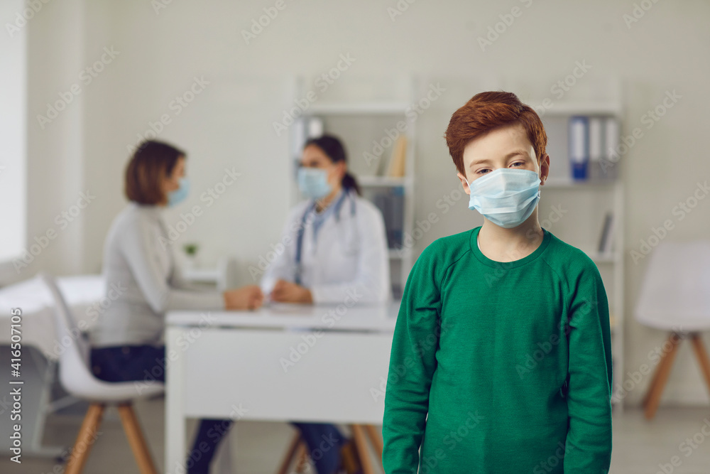 Portrait of little boy wearing face mask. Healthy child in medical mask standing against blurred doctor's office and looking at camera. Concept of healthcare for children and prevention of infection