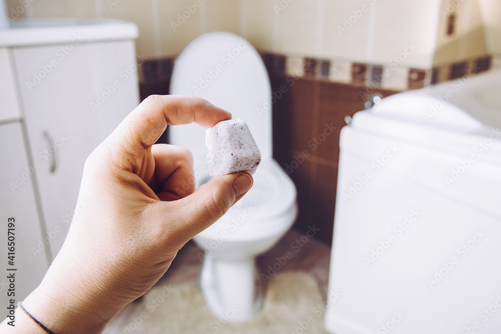DIY toilet fizzie bomb for cleaning home toilet bowl. Selective focus on woman hand, holding homemade natural cleaning pod tablet. Green sustainable lifestyle concept.