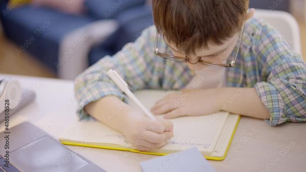 Child in eyeglasses doing homework assignment in notebook, primary school Child in eyeglasses doing homework assignment in notebook, primary school