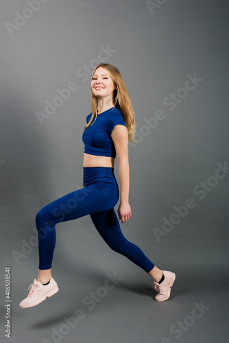 Portrait of young sporty woman smiling while sitting isolated on grey background