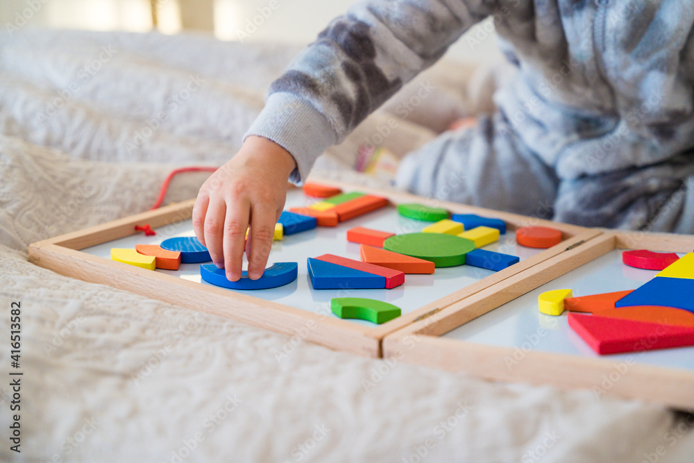 Little toddler  plays on the bed in a wooden magnetic constructor, preschool child learning at home to make mosaic. Early development. Playing with chikldren during coronavirus outbreak.