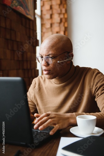 Focused african man wearing headphones watching webinar training making notes study online learning language on computer, black male student looking at laptop elearning in internet write information