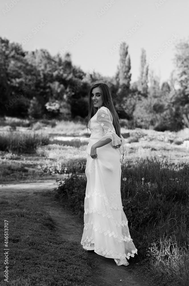 Portrait of young attractive woman in long white wedding dress in spring garden with blooming trees. Spring background. Wedding concept. Greeting card. 