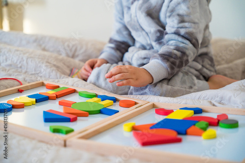 Little toddler plays on the bed in a wooden magnetic constructor, preschool child learning at home to make mosaic. Early development. Playing with chikldren during coronavirus outbreak.