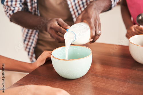 Father carefully putting milk at the plate while preparing breakfast