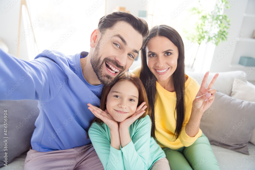 Photo of cheerful young family mom dad daughter happy positive smile show peace cool v-sign sit sofa home Photo of cheerful young family mom dad daughter happy positive smile show peace cool v-sign sit sofa home