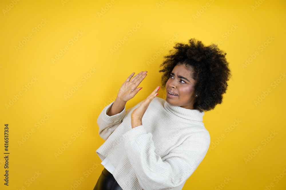 African american woman wearing casual sweater over yellow background scared with her arms up like something falling from above African american woman wearing casual sweater over yellow background scared with her arms up like something falling from above