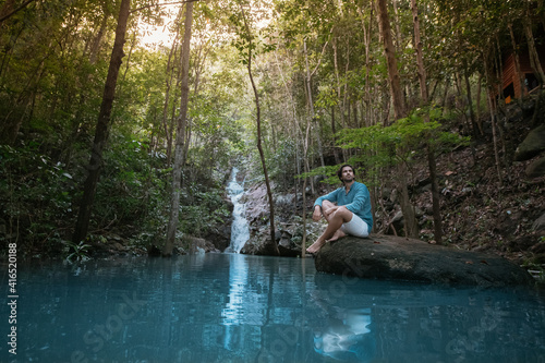 A man sits on a stone in a lake in a tropical forest.