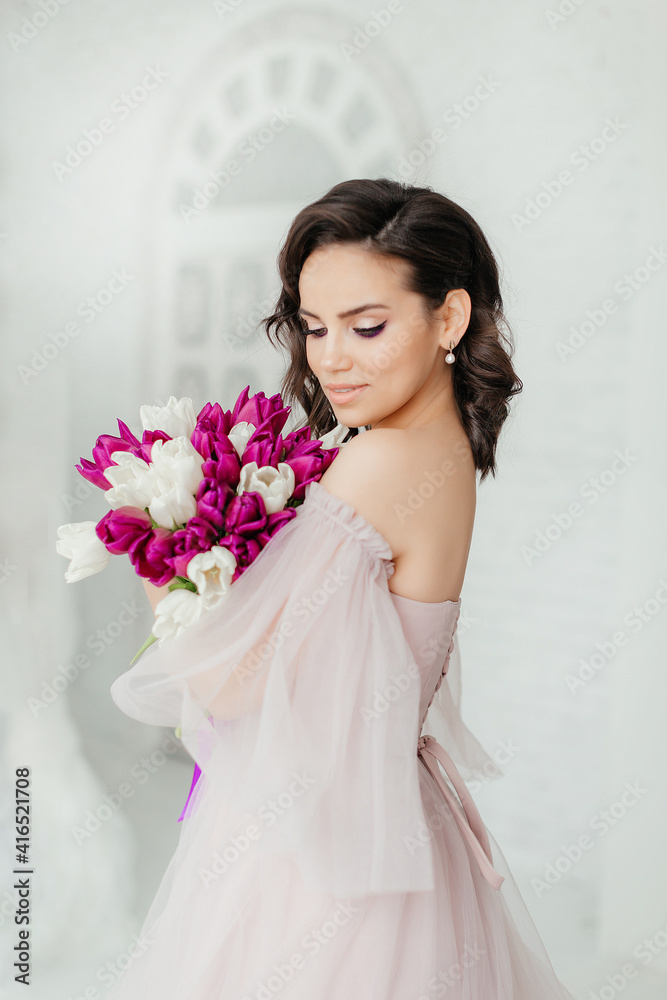 An attractive young woman holds a bouquet of white and purple tulips in her hands. Beautiful girl in a lush dress An attractive young woman holds a bouquet of white and purple tulips in her hands. Beautiful girl in a lush dress