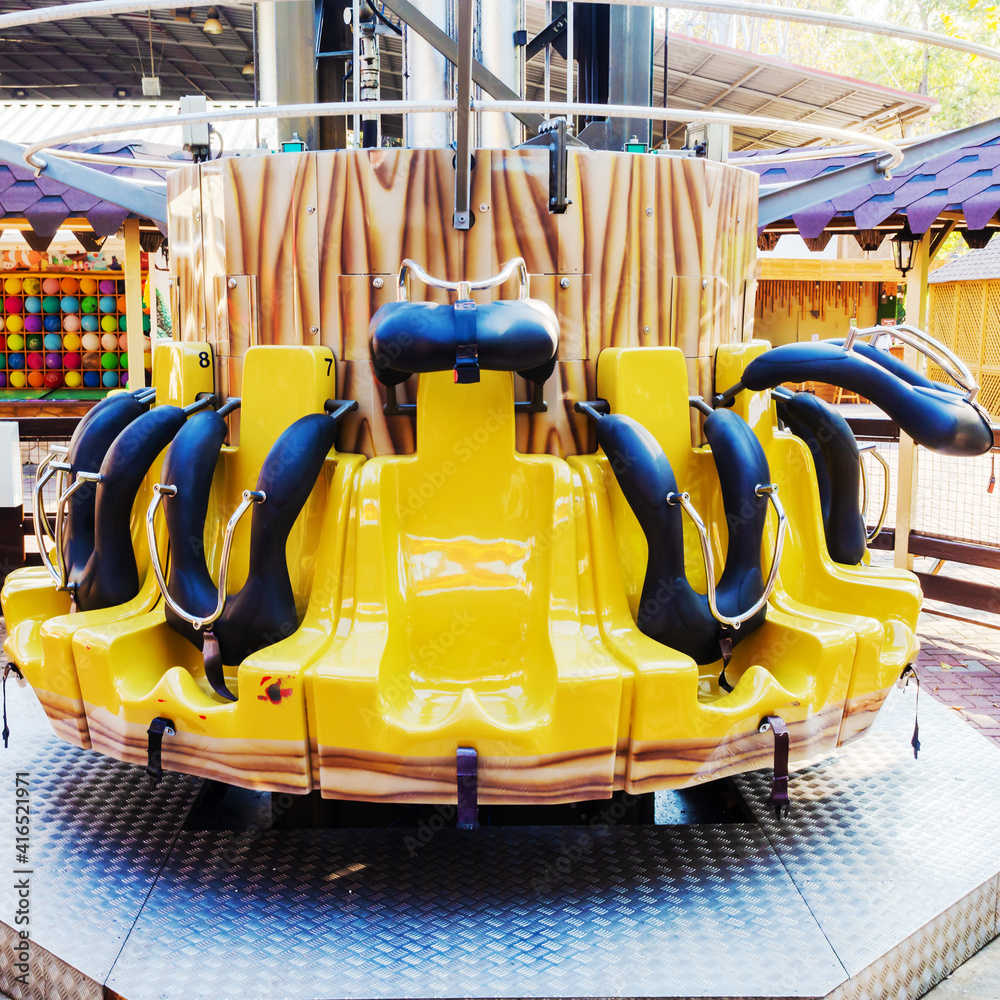 Yellow attraction with empty seats arranged in a circle. Amusement park