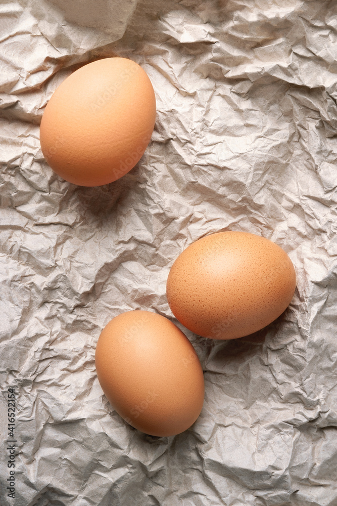 Chicken eggs. Top view of three raw brown chicken eggs on crumpled wrapping paper. High calorie protein food concept. Chicken eggs. Top view of three raw brown chicken eggs on crumpled wrapping paper. High calorie protein food concept.