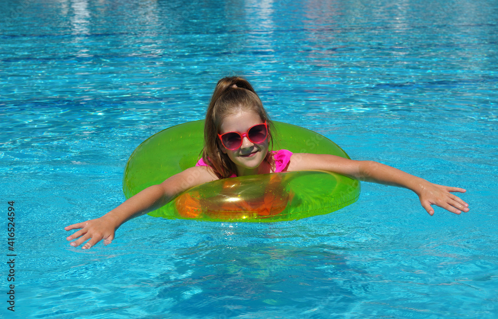 Happy little girl with inflatable ring in swimming pool .
