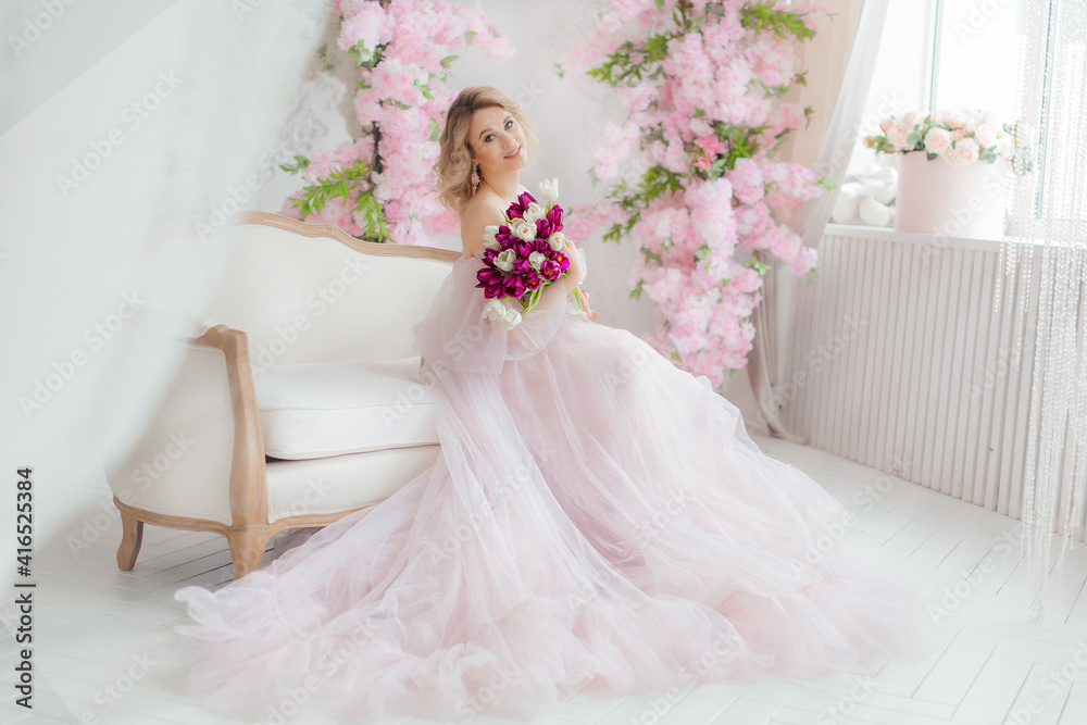 Beautiful girl in a lush pink dress in a photo studio. Bouquet of tulips. Blonde girl with tulips. An attractive young woman holds a bouquet of white and purple tulips in her hands. Beautiful girl in a lush pink dress in a photo studio. Bouquet of tulips. Blonde girl with tulips. An attractive young woman holds a bouquet of white and purple tulips in her hands.