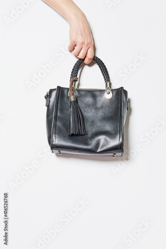 Hand holds handbag over white background. Fashion vogue style shoot of a trendy handbag in female hands against the white wall
