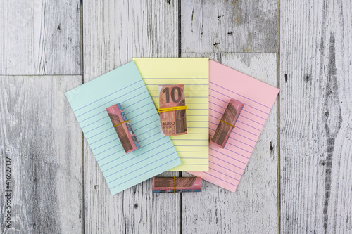Rolls of 10 Euro banknotes on colored notepads arranged fanned to the centre of the screen on a wood background in an overhead view for financial concepts. Flat lay, top view