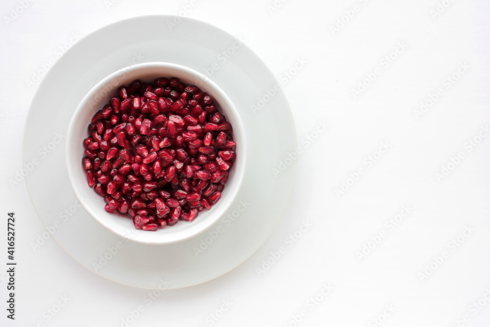 Red pomegranate seeds in a bowl on white table background. Flat lay composition. Healthy food concept. Top view, copy space. Red pomegranate seeds in a bowl on white table background. Flat lay composition. Healthy food concept. Top view, copy space.