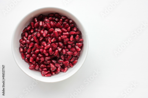 Red pomegranate seeds in a bowl on white table background. Flat lay food composition. Top view, copy space. 