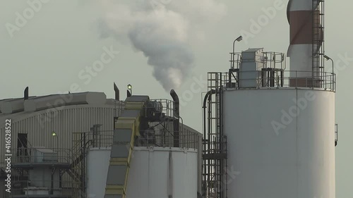 White toxic smoke fumes belch from an industrial factory exhaust chimney. Mid shot. Day time.