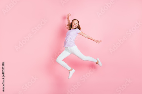 Full length profile side photo of happy cheerful little girl raise hands isolated on pastel pink color background