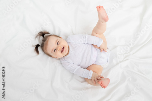 baby lying on the bed at home on a white bed with his feet up, the concept of a happy loving family and children