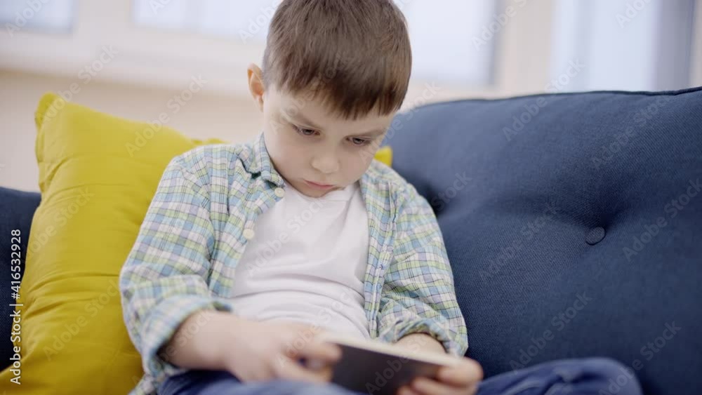Upset little boy playing smartphone game on sofa, feeling lonely, behavior Upset little boy playing smartphone game on sofa, feeling lonely, behavior