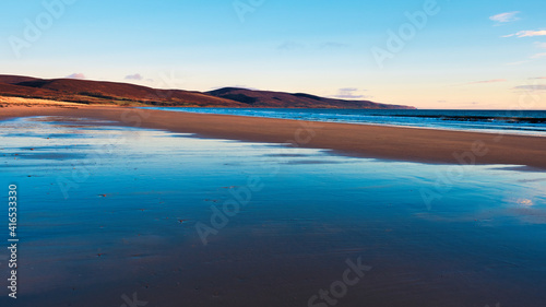Brora beach in the Highlands of Scotland with blue skies and reflections in the wet sand