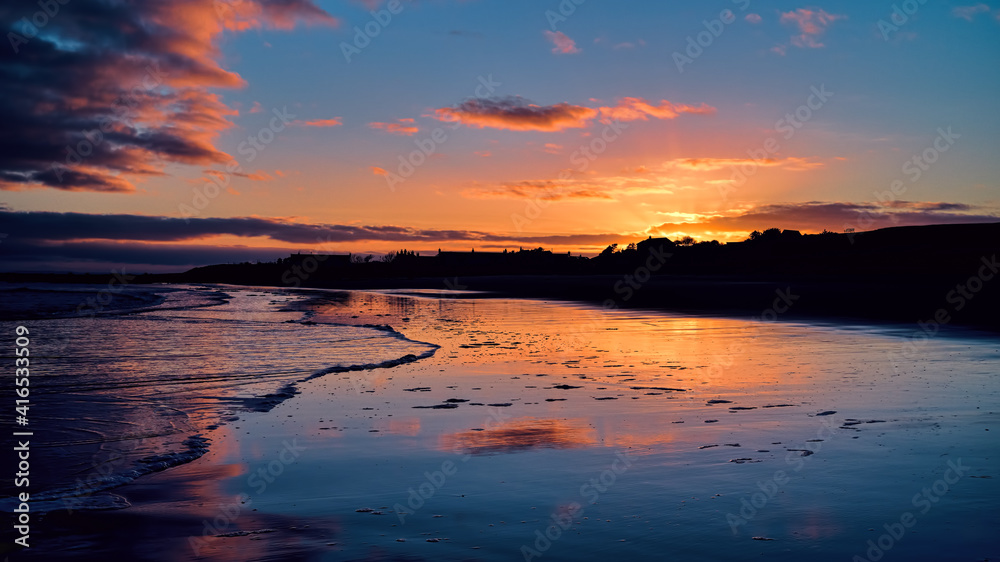 Winter golden sunset on Brora beach in the Highlands with reflections in the wet sand