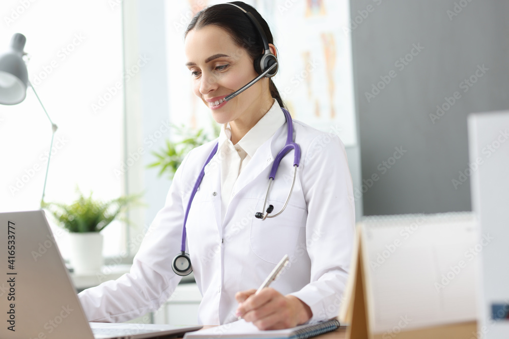 Woman doctor with headset looking into laptop screen Woman doctor with headset looking into laptop screen