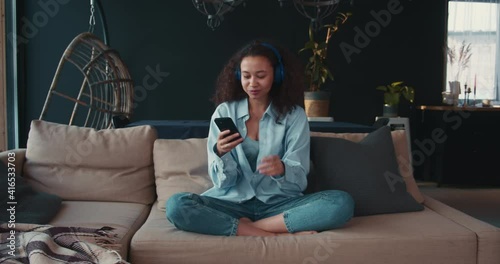 Music streaming app. Beautiful young happy African American student woman listening, dancing to music in headphones.