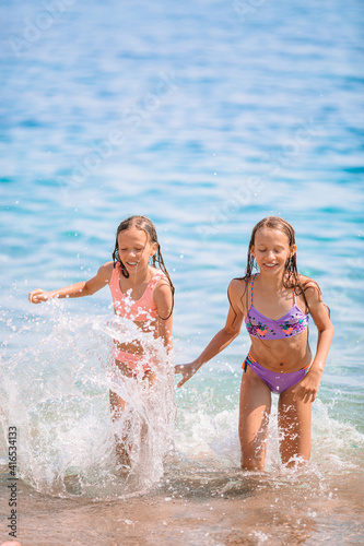 Happy children splashing in the waves during summer vacation on tropical beach. Girls play at the sea.