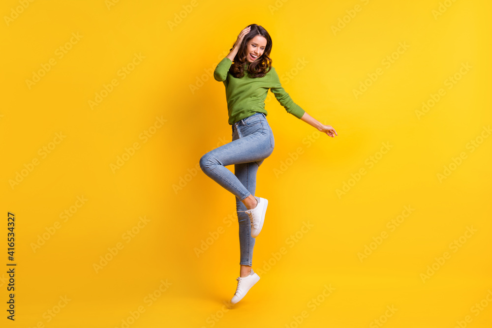 Full size photo of gorgeous active young woman wear jeans touch hair jump up isolated on vibrant yellow color background
