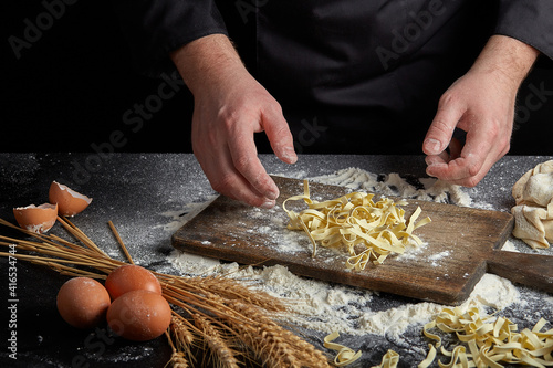 Homemade raw noodles made from flour, egg on wooden bowl on black. Chef hands