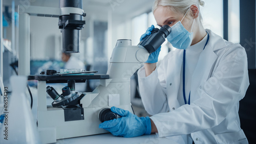 Modern Medical Research Laboratory: Portrait of Female Scientist Wearing Face Mask Looking Under Microscope, Analysing Test Samples. Advanced Scientific Lab for Medicine, Microbiology Development