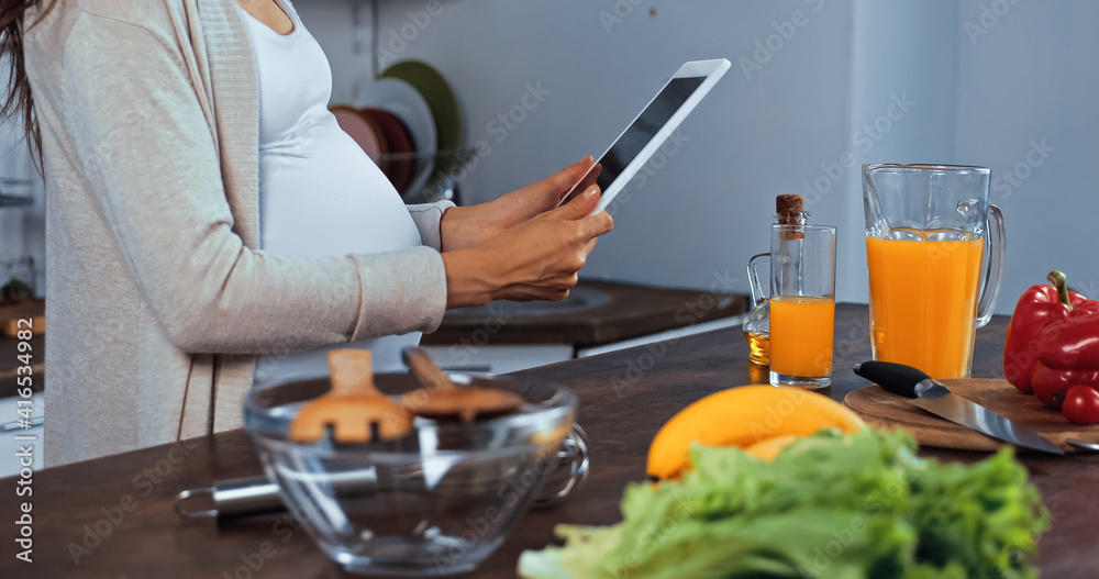 Cropped view of pregnant woman holding digital tablet near fresh food Cropped view of pregnant woman holding digital tablet near fresh food
