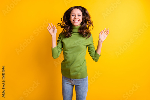 Photo of young happy smiling cheerful good mood woman showing palms with flying hair isolated on yellow color background