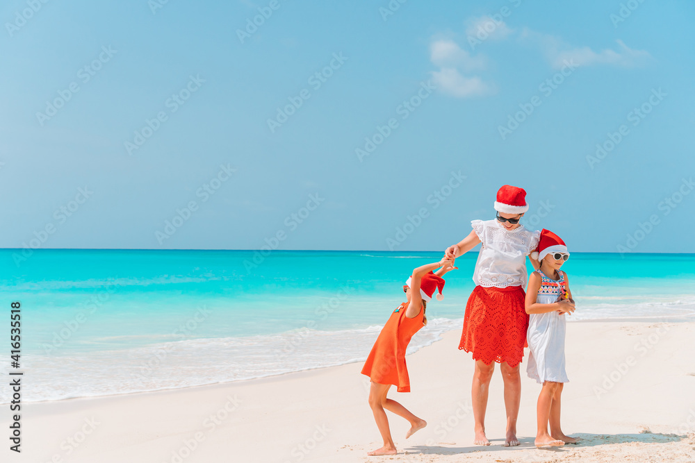 Adorable little girls and young mother on tropical white beach on Christmas vacation