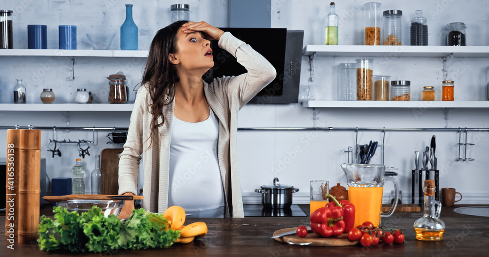 Amazed pregnant woman standing near fresh food and orange juice on kitchen table Amazed pregnant woman standing near fresh food and orange juice on kitchen table
