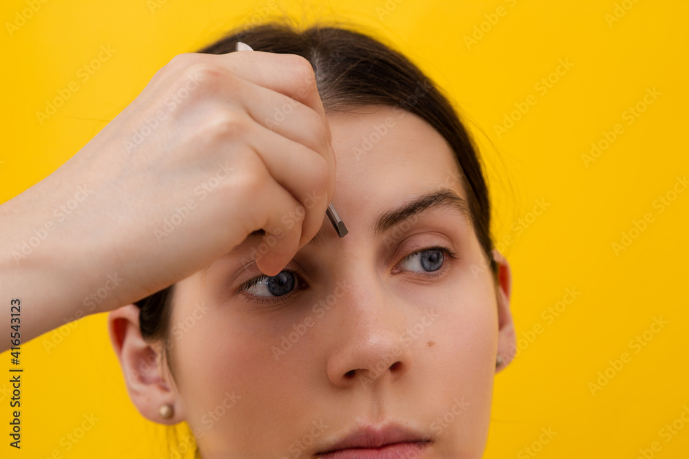 Portrait of young woman plucking eyebrows with tweezers