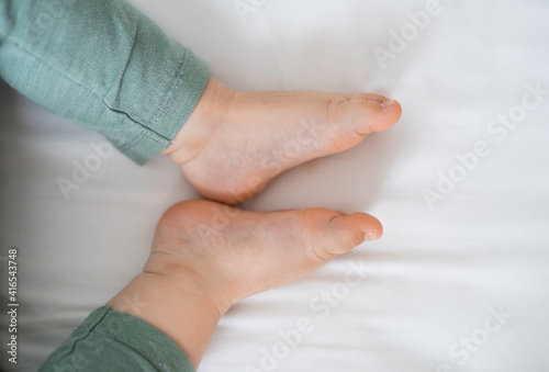 baby foot feet, bare heels, green pants, on a white sheet top view