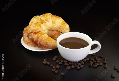 Croissants on a plate with a cup of espresso coffee and coffee beans on black background