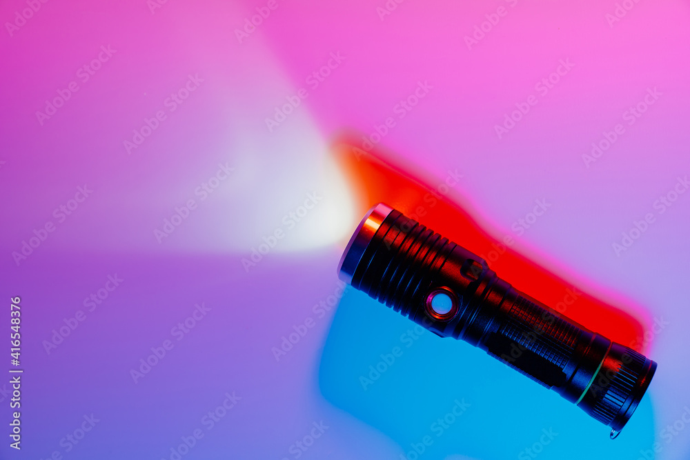 A small black flashlight in colored lighting. A small black flashlight in colored lighting.