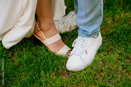 men's feet in white sneakers and women's legs in sandals on green grass. 
