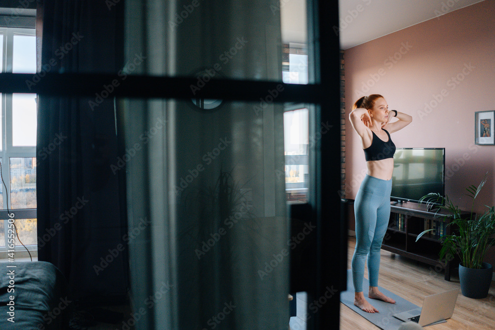 Remote side view of fit woman doing stretching exercise for arms and shoulder muscles at home. Concept of sports training red-haired lady during quarantine. Remote side view of fit woman doing stretching exercise for arms and shoulder muscles at home. Concept of sports training red-haired lady during quarantine.